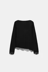 Top de manga larga en tejido suave color gris, con cuello redondo y bajo asimétrico decorado con encaje negro a tono. Presenta detalles de encaje negro en los puños.