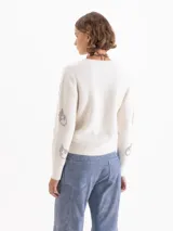 Sweater de tejido de punto gris con textura de pelo, cuello redondo y mangas largas. Presenta un bordado frontal de piedras brillantes con forma de flamas.