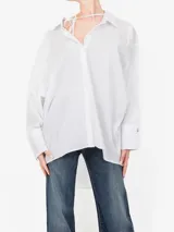 Camisa de corte oversize confeccionada en algodón, con cuello clásico y detalle de lazo ajustable en la zona superior. Presenta mangas largas con puños anchos y un diseño asimétrico con la parte trasera más larga que la delantera.