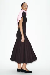 Vestido midi de color negro, confeccionado en tejido de punto con cuello barco y manga corta. Presenta un diseño ajustado en el torso que se combina con una falda inferior con vuelo y acabado evasé.