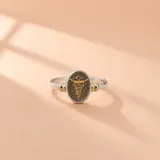 Anillo de plata 925 y oro 18k con diseño ovalado frontal que presenta el símbolo del caduceo de la medicina en relieve dorado sobre fondo texturizado. Cuenta con detalles dorados a los lados del cuerpo de la sortija.