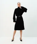 Blusa Cortelle estilo bata, color negro, con cuello alto fruncido, cierre posterior y mangas largas amplias tipo campana con volados en capas.