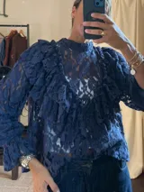 Camisa de encaje azul marino con cuello alto, mangas largas con puños acampanados y volados frontales decorativos.