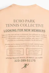 Remera color salmón de corte holgado, confeccionada en algodón, con cuello redondo y estampa pequeña en el pecho con la inscripción 'Echo Park Tennis Collective' y la silueta de un tenista.
