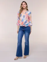 Blusa estampada Zac & Rachel con diseño floral en tonos rosados, azules y amarillos sobre base blanca. Presenta escote en V con botones frontales, mangas tres cuartos con presilla para arremangar y detalle de nudo en el ruedo.
