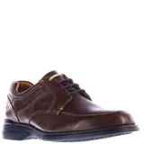 Zapato de vestir para hombre color marrón chocolate, confeccionado en cuero con textura granulada. Presenta costuras decorativas en contraste, cierre con cordones y suela de goma negra con tecnología de amortiguación.