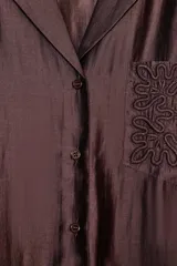 Camisa de manga larga color marrón oscuro, con cuello solapa, escote pico y bajo asimétrico. Presenta un bolsillo plastrón en el delantero con bordado combinado a tono.