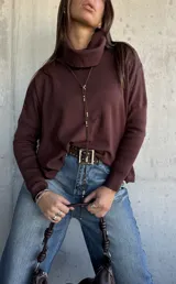 Sweater de tejido de punto color chocolate, con cuello polera, mangas largas con puños acanalados y diseño holgado con aberturas laterales y detalle de botones.