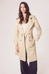 Trench color beige con doble botonadura, cinturón y cuello clásico.