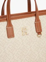 Cartera tote Tommy Hilfiger modelo TH Monoplay, color beige con estampado integral del monograma TH en relieve, asas superiores y correa bandolera extraíble de cuero sintético marrón. Cuenta con cierre de cremallera e insignia metálica del monograma en el frente.