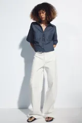 Camisa crop color blanco confeccionada en mezcla de lino, con cuello solapa, escote en pico, mangas cortas con trabilla, bolsillos de plastrón en el pecho y cierre frontal con botones.