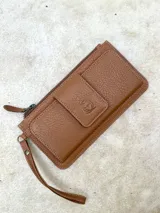 Billetera de cuero color marrón con cierre de cremallera y correa de muñeca. Cuenta con un bolsillo frontal con solapa y cierre a presión con el logo de la marca.