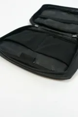 Bolso portadocumentos negro rectangular con cierre de cremallera y detalle de costura diagonal en el frente. Incluye logo "DREAM" en la parte inferior.