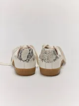 Championes de cuero color blanco con puntera y suela de goma marrón claro. Presentan detalles bordados dorados en los laterales y cordones anchos en color crudo.