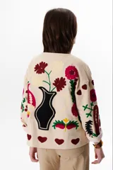 Chaqueta color crudo con bordados florales en tonos rojo, verde y negro.