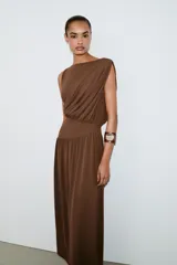 Vestido largo sin mangas de cuello redondo, confeccionado en tejido drapeado con detalle de cintura tipo fajín en el mismo material.