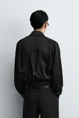 Cazadora bomber negra con textura arrugada, cuello solapa, hombreras marcadas, manga larga con puño abotonado, bolsillos de vivo en la cadera, bajo elástico y cierre frontal con cremallera.