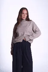 Sweater color beige de tejido de punto con cuello alto y mangas largas. Presenta detalles de ochos en diagonal en los laterales.