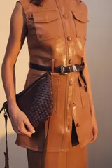 Bandolera de gamuza color marrón con diseño de media luna, decorada con tachas metálicas doradas distribuidas en el frente. Cuenta con cierre superior metálico y correa larga ajustable para llevar cruzada.
