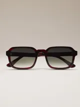 Lentes de sol de montura gruesa, estilo cuadrado, color carey oscuro (rojo/negro). Lentes oscuros con degradado grisáceo.