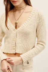 Cardigan de punto color beige, con escote en V y cierre frontal de botones, de mangas largas y corte corto.