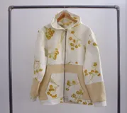 Canguro con capucha y cierre frontal, color beige con estampado de hojas en tonos marrones y amarillos. Mangas largas en color gris.