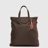 Mochila convertible en bolso tipo tote de la marca Bubba, color marrón, con acabado impermeable. Presenta un diseño minimalista con solapa frontal, doble asa superior y un llavero decorativo con la letra B en color rosado.