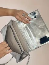 Sobre de cuero color plateado con correa fina blanca y cierre superior.