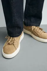 Zapatillas de cordones color beige, fabricadas en piel con acabado serraje. Presentan detalles de pespuntes en la parte superior y suela plana a contraste color crema.