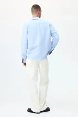 Camisa de algodón Oxford con cuello americano, bolsillo frontal y mangas largas con puños abotonados. Presenta un corte estándar y bajo redondeado.