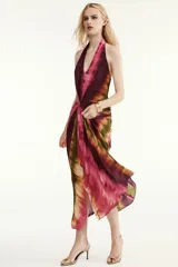 Vestido midi de cuello halter y escote en V, con diseño tie-dye en tonos fucsia, borgoña y verde. Presenta un nudo decorativo en el delantero, espalda descubierta y abertura frontal en el bajo.