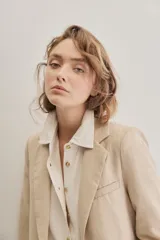 Blazer sastrero de lino color beige, de silueta relajada y líneas clásicas. Incorpora solapas tradicionales, cierre frontal de un botón y bolsillos de vivo.
