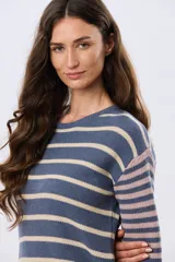 Buzo tejido de algodón con diseño a rayas horizontales, cuello redondo y mangas largas. El cuerpo presenta rayas en tonos azul y beige, mientras que las mangas combinan rayas en tonos azul y rosado.