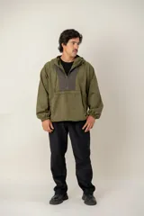 Canguro con capucha de estilo urbano en color verde oliva, confeccionado en tejido suave. Presenta un panel frontal en contraste de color gris oscuro con cierre de cremallera parcial, mangas largas con puños elásticos y bolsillos laterales integrados.