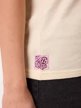 Remera blanca de corte holgado, con cuello redondo y mangas cortas. Presenta un pequeño estampado en el pecho con diseño floral y tipografía.