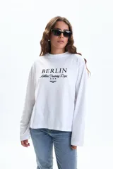 Remera blanca de manga larga con cuello redondo y estampado frontal que dice "BERLIN Athletic Training Dept." con tres estrellas y "URBAN LEGACY 1986" debajo.