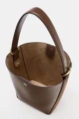 Bolso tipo saca con diseño estructurado, confeccionado en una combinación de cuero liso y gamuza en tono marrón. Cuenta con asa de hombro fija, cierre imantado y detalles metálicos en dorado.