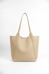 Bolso tipo tote de diseño minimalista, confeccionado en material texturizado color beige, con doble asa larga para llevar al hombro y costuras reforzadas en los laterales.