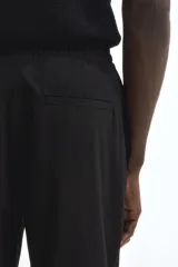 Pantalón tipo jogger de vestir, corte slim fit, con cintura elástica y cordón de ajuste. Presenta pliegues frontales y traseros, bolsillos laterales al bies y bolsillos traseros insertados.