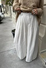 Pantalón sastrero color crudo, de corte amplio, con botón, pasacinto y pretina trasera con elástico.