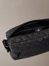 Bolso cruzado rectangular de color negro con estampado de monograma en tono gris oscuro. Cuenta con correa ajustable de tela negra y un tirador de cremallera de cuero negro.