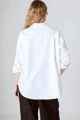 Camisa blanca de corte clásico, con cuello camisero y mangas largas con puños abotonados.