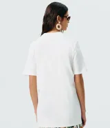 Remera de algodón blanca de corte largo, manga corta y cuello redondo. Presenta un gran estampado floral en tonos azules con la inscripción "Botanist" en el frente.