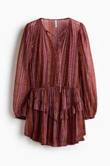 Vestido corto de manga larga confeccionado en tejido transparente, con estampado estilo paisley en tonos borravino y rosado. Presenta cuello redondo con abertura frontal y cordones para atar, cintura elástica y falda con volados en capas.