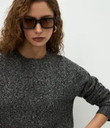 Suéter de punto jaspeado en color gris oscuro, con cuello redondo y mangas largas. Presenta un diseño integrado con una camisa blanca debajo, creando un efecto de capas superpuestas.