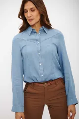 Camisa de jean en tono celeste claro, con cuello clásico, cierre frontal de botones y costuras frontales verticales que definen la silueta.
