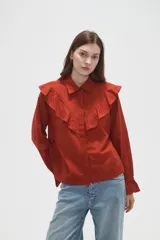 Camisa de algodón blanca con cuello camisero, cierre frontal de botones y volados bordados en el frente y hombros. Presenta mangas largas con puños acampanados y detalles bordados en el ruedo.