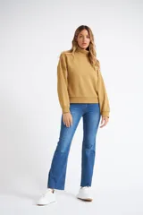 Buzo tipo polera de algodón, con cuello alto, mangas largas con puños y diseño holgado. Presenta una pequeña grifa metálica decorativa.