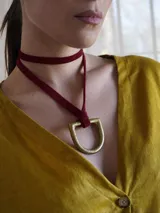 Collar tipo gargantilla con tira de gamuza roja y dije metálico dorado en forma de estribo.