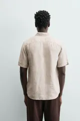 Camisa de lino color beige de corte relajado, con cuello solapa, manga corta y cierre frontal con botones.